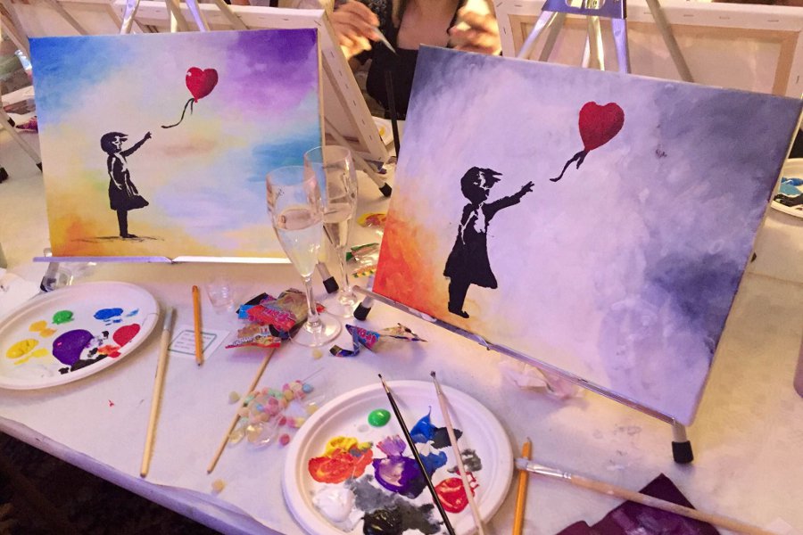 Zwei selbst gemalte Bilder mit einem Banksy-Motiv auf einem Tisch mit Farben