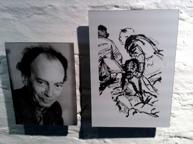 Das Foto eines Mannes hängt neben einer Zeichnung, auf der zwei Uniformierte einen halb Bewusstlosen hinter sich herzerren